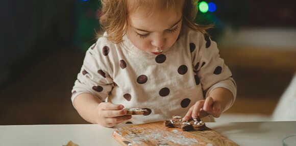 Niña haciendo y comiendo galletas sola.